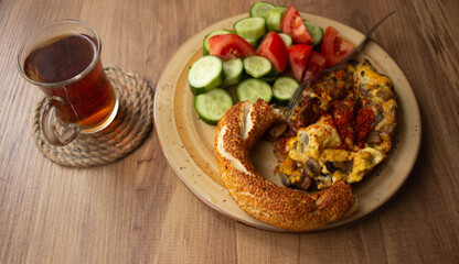 Selective focus, traditional Turkish tea in tea glass and Turkish bagel, tomato slices, cucumber slices in the plate on a wooden table. daylight comes through the window
Turkish breakfast, alone 