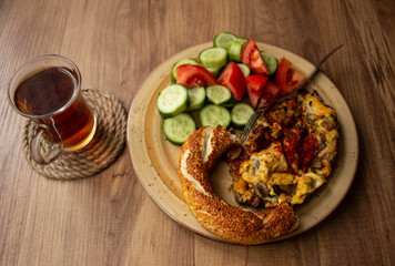 Selective focus, traditional Turkish tea in tea glass and Turkish bagel, tomato slices, cucumber slices in the plate on a wooden table. daylight comes through the window
Turkish breakfast, alone 