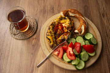 Traditional Turkish tea in tea glass and Turkish bagel, tomato slices, cucumber slices in the plate on a wooden table. daylight comes through the window
Turkish breakfast, alone 