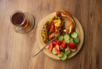 Selective focus, traditional Turkish tea in tea glass and Turkish bagel, tomato slices, cucumber slices in the plate on a wooden table. daylight comes through the window

