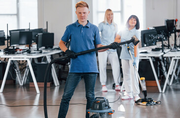 Guy with vacuum cleaner. Group of workers clean modern office together at daytime