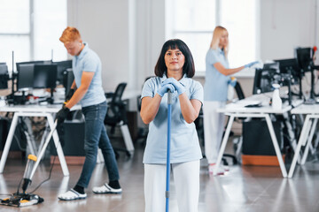 Cleans floor. Group of workers clean modern office together at daytime