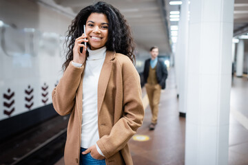 happy african american woman talking on smartphone near man in subway on blurred background