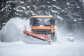 Snowplow clearing road from snow in the forest with traffic lining up behind the truck