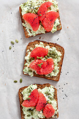 Toasts with rye bread, avocado, cottage cheese, grapefruit, and pumpkin seeds on a grey background. Top view. Tasty and healthy breakfast or snack. Vegetarian food.