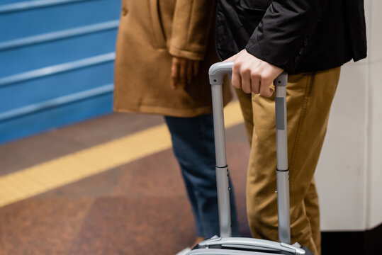 partial view of couple standing on platform of subway with luggage