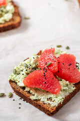 Toasts with rye bread, avocado, cottage cheese, grapefruit, and pumpkin seeds close-up. Free space for text. Tasty and healthy breakfast or snack. Vegetarian food.