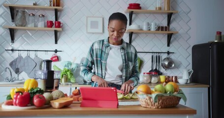Young african cheerful woman chef making online class videoconference via tablet computer showing cooking skills expliaining recipe in the kitchen. - Powered by Adobe