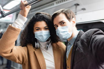 multicultural couple in medical masks in wagon of metro