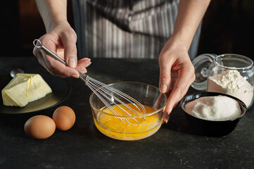 The process of preparing the dough. The woman whips the egg mixture with a whisk against a dark...