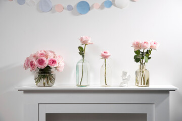 Bouquet of pink roses in a glass figured vase on a white fireplace console. A faience figurine of two pears and a bird as an interior decoration. Copy space. Rose White Pink O'hara.