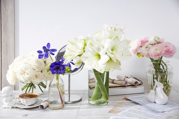 White roses, ranunculus, blue anemones, yellowish buttercups, lilies in round vases on the wooden boxes on the table for a special occasion as a kitchen decoration.