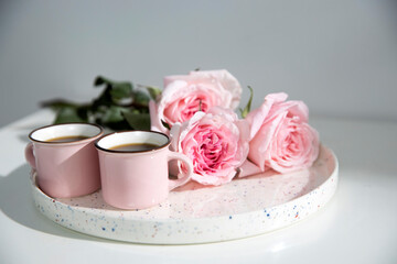 Obraz na płótnie Canvas Two small pink cappuccino cups with three pink roses on a tray on a coffee table