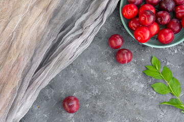 Top view of fresh organic ripe plums in ceramic bowl decorated with grey gauze fabric, leafs, copy space. Flat lay. High quality photo