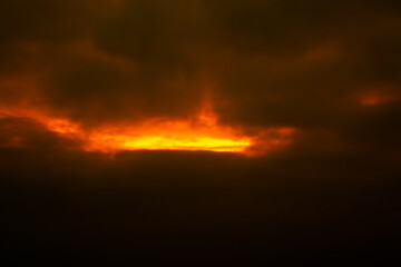Dark fiery sunset fog with bright fiery sunlight shining through black clouds.