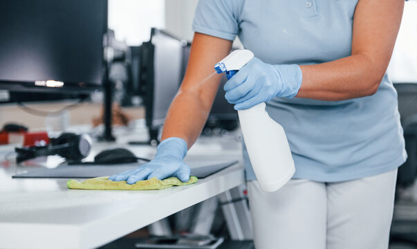 Close up view of woman in protective gloves that cleaning tables in the office