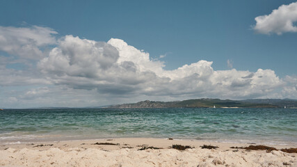 Beach coastline with white sand, crystal clear waters and clouds in the sky. Cíes Islands Beach