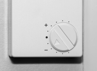 Simple wall mounted white thermostat dial for adjusting room temperature. Close up.