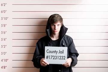 arrested prisoner young man holding a placecard in front of the height chart