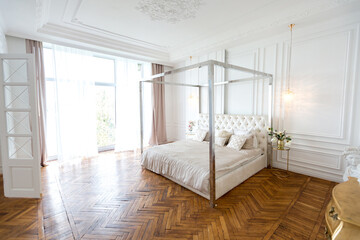 modern interior of a luxurious large bright bedroom. white stucco walls and a large four-poster bed and wooden parquet floor