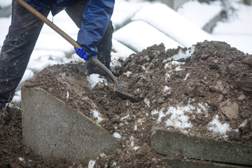 Details of a gravedigger covering a tomb with dirt with a shovel during a burial ceremony on a cold and snowy winter day.