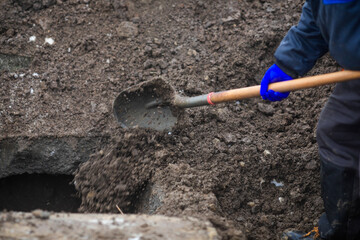 Details of a gravedigger covering a tomb with dirt with a shovel during a burial ceremony on a cold...