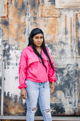 Beautiful and serious African American teenage girl with long hair and a pink magenta jacket standing  outside in an urban city setting © Ursula Page