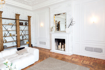 modern interior of a luxurious large bright living room. white expensive sofa and wooden shelving, white walls with moldings and a luxurious chandelier