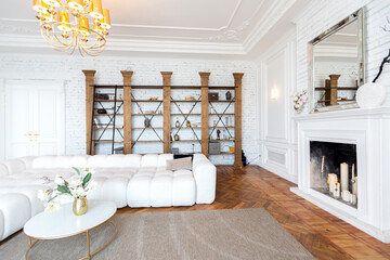 modern interior of a luxurious large bright living room. white expensive sofa and wooden shelving, white walls with moldings and a luxurious chandelier