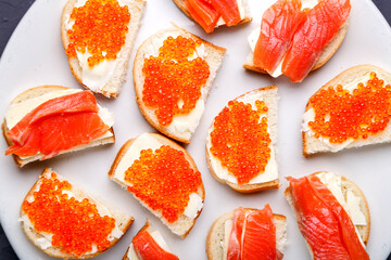 Bruschettes with butter and red caviar and salmon on a white plate.