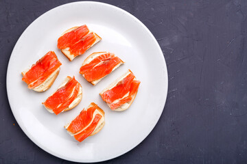 Bruschettes with butter and salmon on a white plate on a gray concrete background. Copy space.