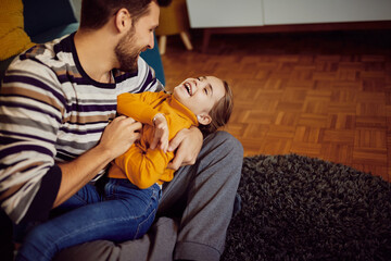 Happy father tickling his daughter and having fun at home.