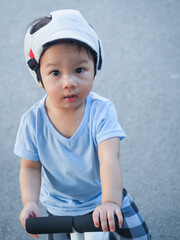 Cute baby asian boy wear Safety Helmet Headguard learning to ride his first white running bike on road.