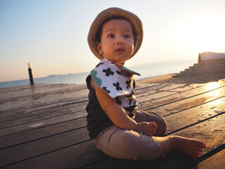 portrait of asian baby boy sit on the wood floor near beach,evening,sunset