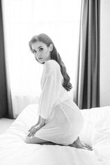 black and white.beautiful woman with makeup, long hair sits in white robe on bed