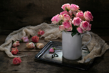 A bouquet of pink roses in a white jug on a wooden background.