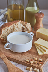 Close-up of cheese cream puree soup on a white table. Next around the ingredients: mushrooms, onions, crackers, bread, cheese, milk and butter. Rustic style