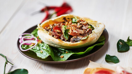 Close up of flatbread pita withwith vegetables and meat at the wodden white table. Fried ohnny cake. Eastern cuisine. Asia flapjack. Rustic stile.