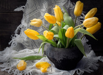 A bouquet of yellow tulips in a vintage jug on a wooden table.