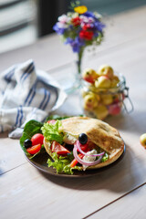 Close up of flatbread pita with vegetables, cucumber, tomato, red pepper at the wodden white table. Fried ohnny cake. Eastern cuisine. Asia flapjack. Rustic stile.