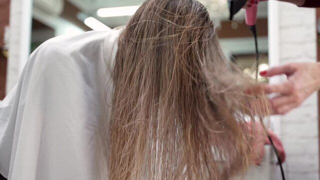 hairdresser's hands blow dry the girl's long blonde hair with her head down