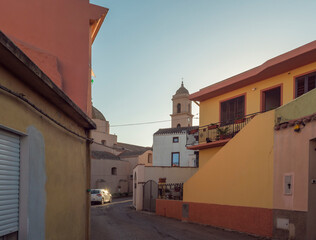 Street in old town of Tortoli with church tower and yellow pink houses. Sardinia, Italy, summer afternoon