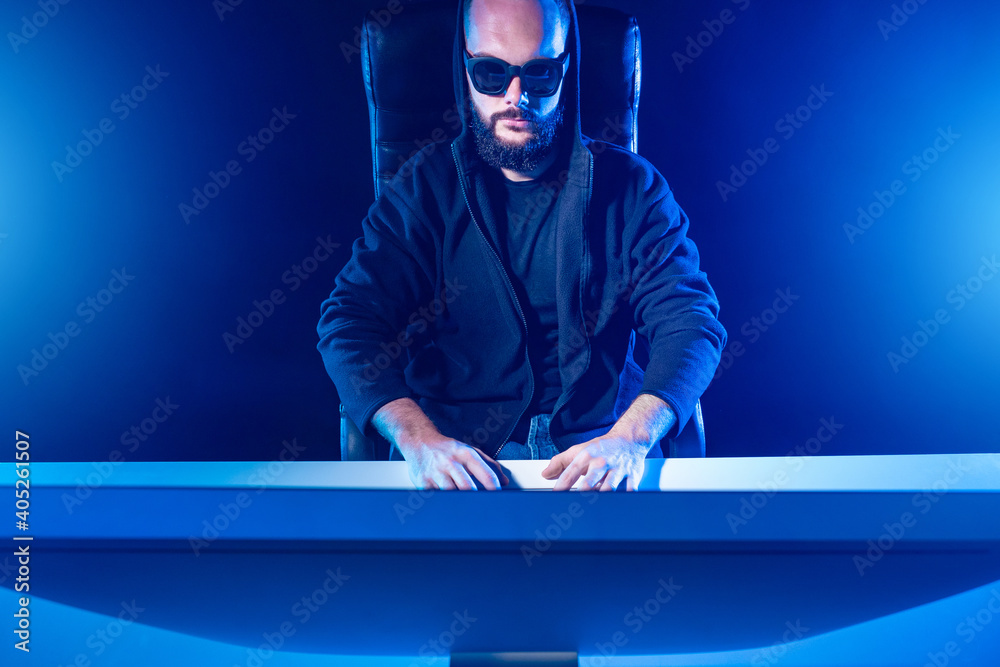 Poster Computer cracker. Hacker in sunglasses. Hacker works in a dark room. Hacker programs looking into the monitor. Hacking computer systems. Geek works until late. Computer cracker man in blue light
