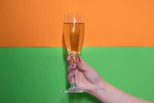 glass of champagne with an engagement ring inside on bright green and orange background. wedding concept. engagement. bride. poping the question.