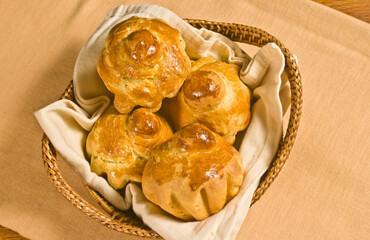 top view, close up of four, freshly baked, brioche, in a tan napkin,  in a wicker, wood basket, on wood cutting board
