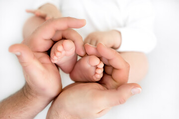 little feet in daddy's hands. dad holds the baby's legs. The legs of the newborn are folded in the shape of a heart. Family Day