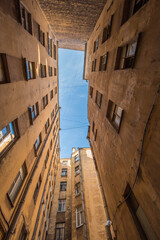 Bottom-up view from a narrow courtyard surrounded by multi-storey buildings. The blue sky above the courtyard is lined with intersecting wires. European city. No people
