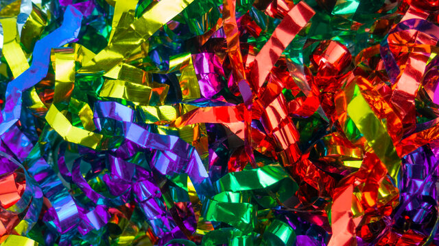 Abstract background close up colorful holiday metal ribbons.Foil serpentin of firecrackers.Red,blue,yellow,green,purple,lilac celebration tapes.Concept of congratulation,festive event,fun.Copy space