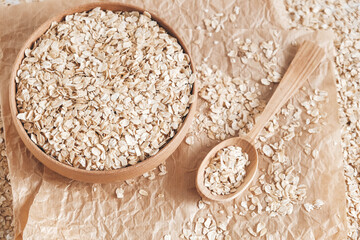 Uncooked oatmeal in a wooden bowl and spoon on kraft paper background. Copy, empty space for text