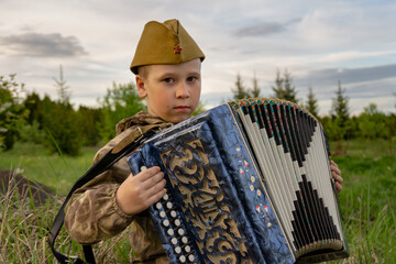 A boy in a military uniform holds an accordion in his hands. Victory Day. 9th May. A Great Victory.